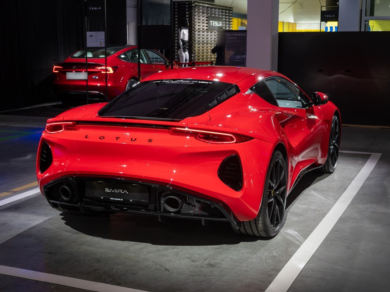 Lotus Emira rossa, vista posteriore di tre quarti a un salone