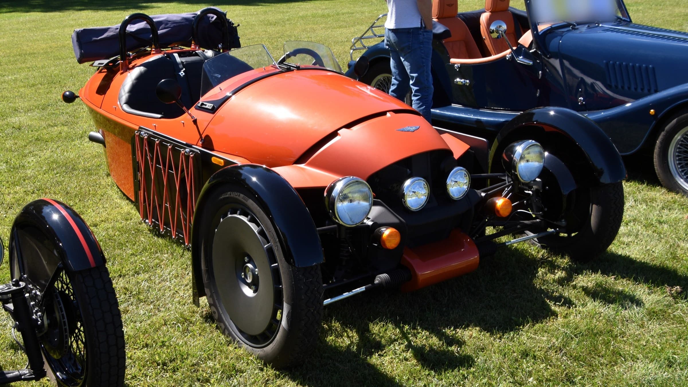 Morgan Super 3 arancione, vista anteriore di tre quarti su un prato