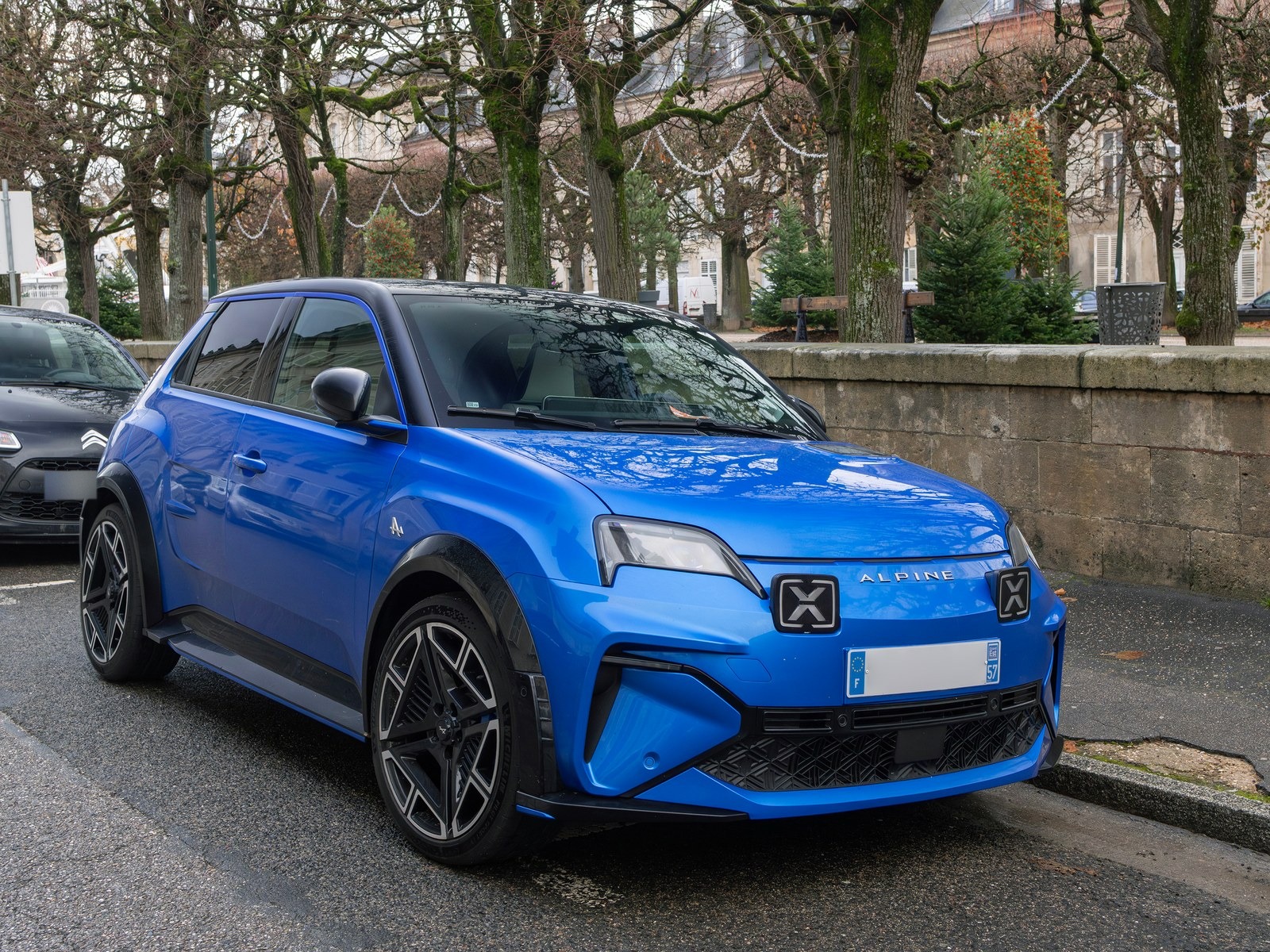 Alpine A290 blu con tetto nero, vista anteriore di tre quarti in una piazza alberata