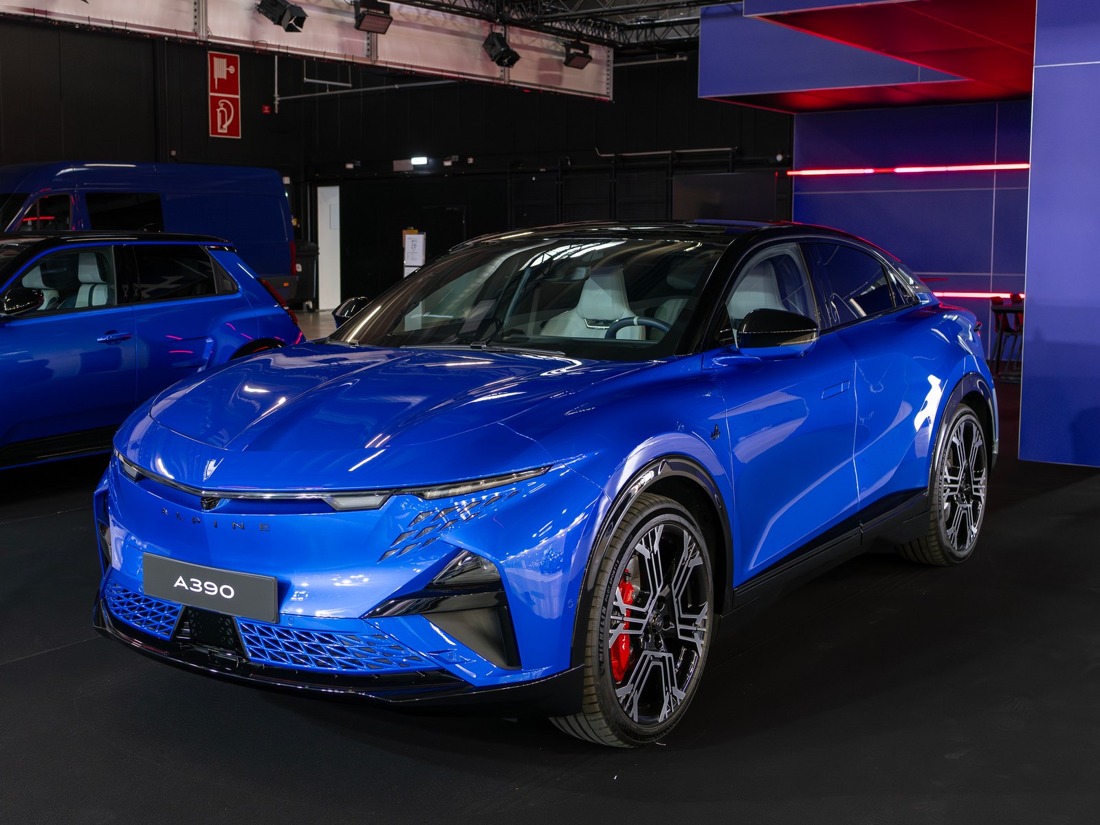 Alpine A390 blu con tetto nero, vista anteriore di tre quarti in un padiglione espositivo