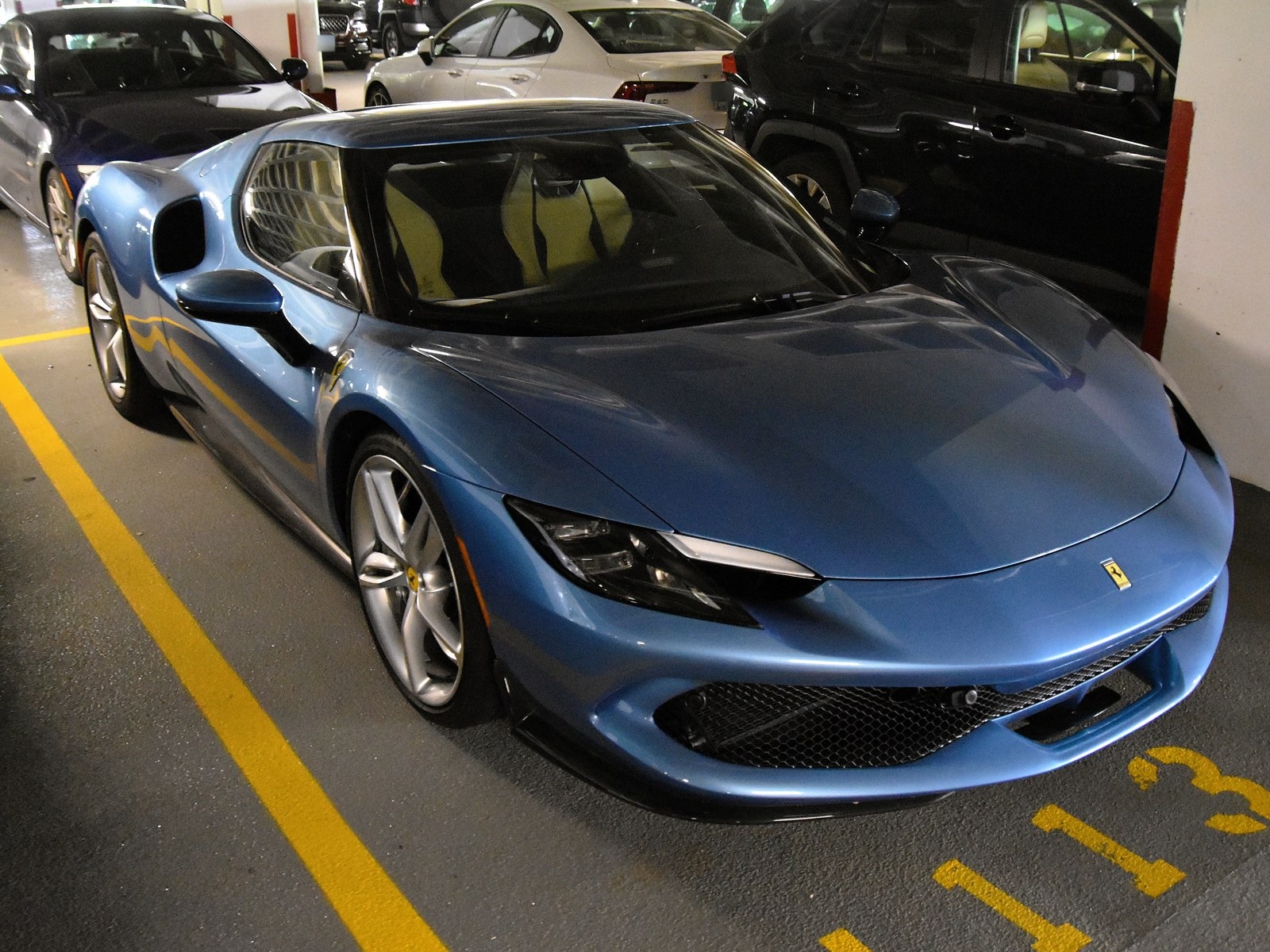 Ferrari 296 GTB azzurra, vista anteriore di tre quarti in un parcheggio coperto