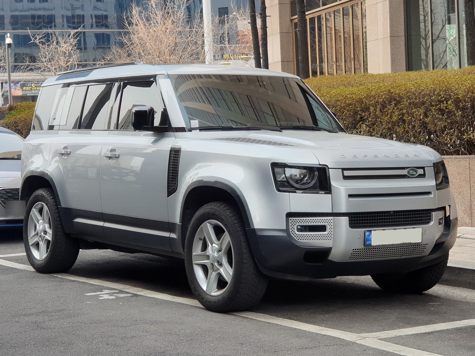 Land Rover Defender 110 argento, vista anteriore di tre quarti in un parcheggio in città