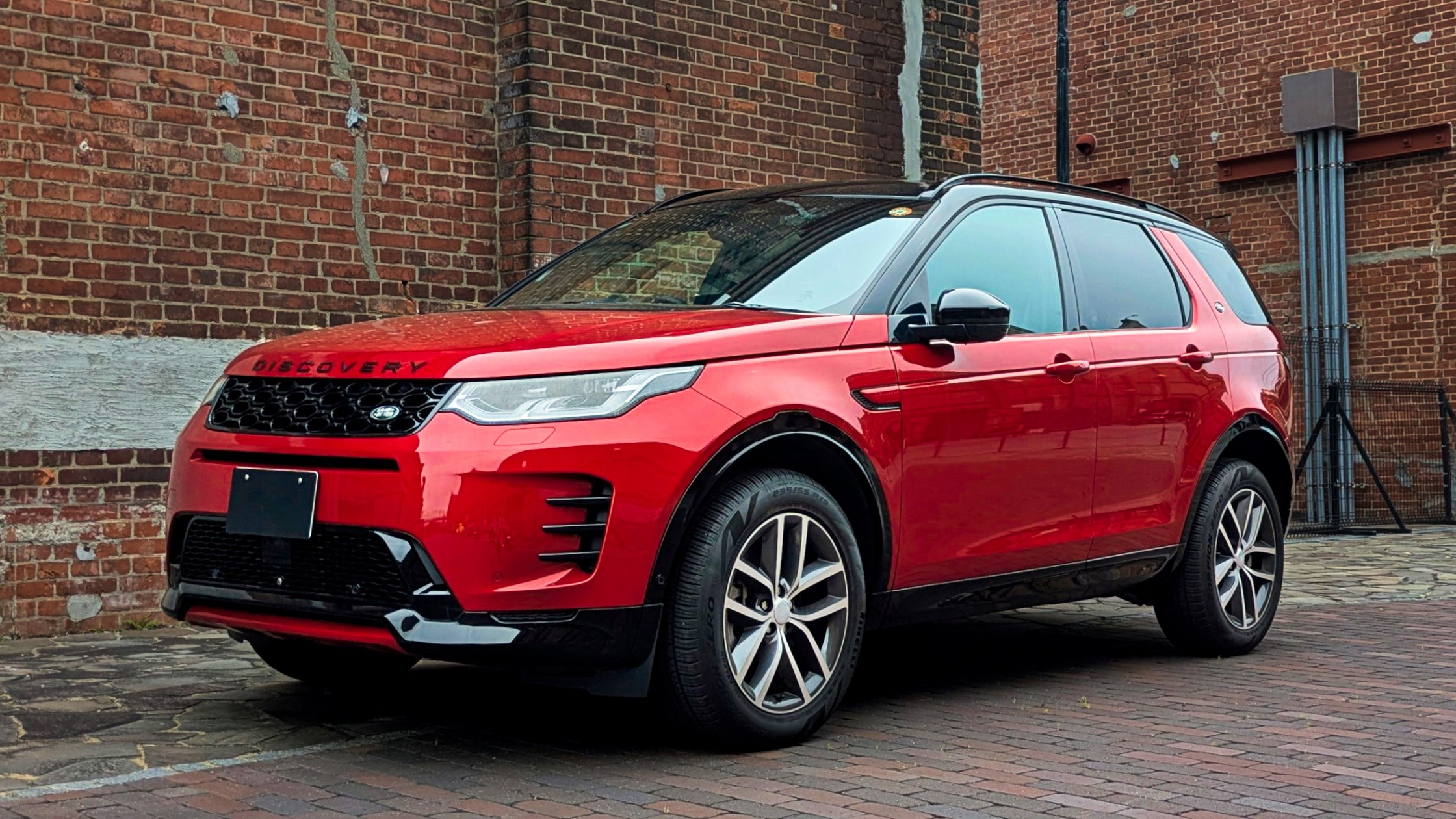 Land Rover Discovery Sport rossa, vista anteriore di tre quarti davanti a un muro di mattoni